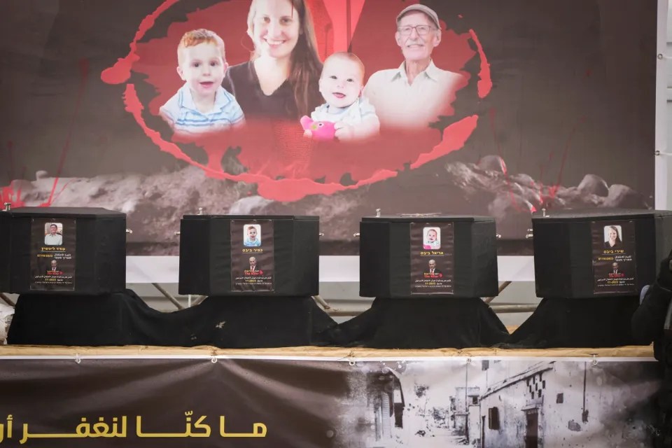 Four caskets with photos of victims displayed in front of a banner showing a family.