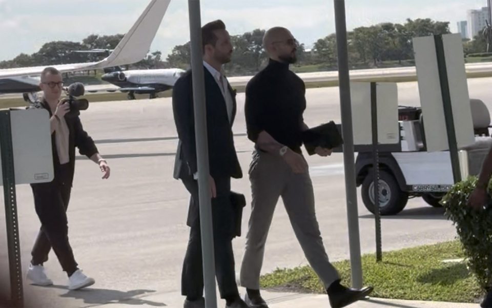 Two men in suits walking at an airport, a photographer taking pictures.