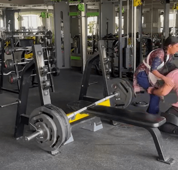 Woman helping man with weightlifting in a gym.