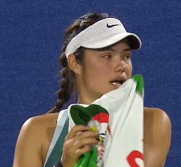 A female tennis player wiping her face with a towel.