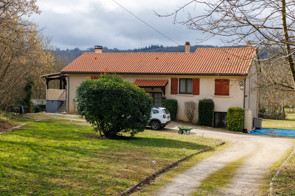 Tan house with a red tile roof, a white car parked in front, and a wheelbarrow.