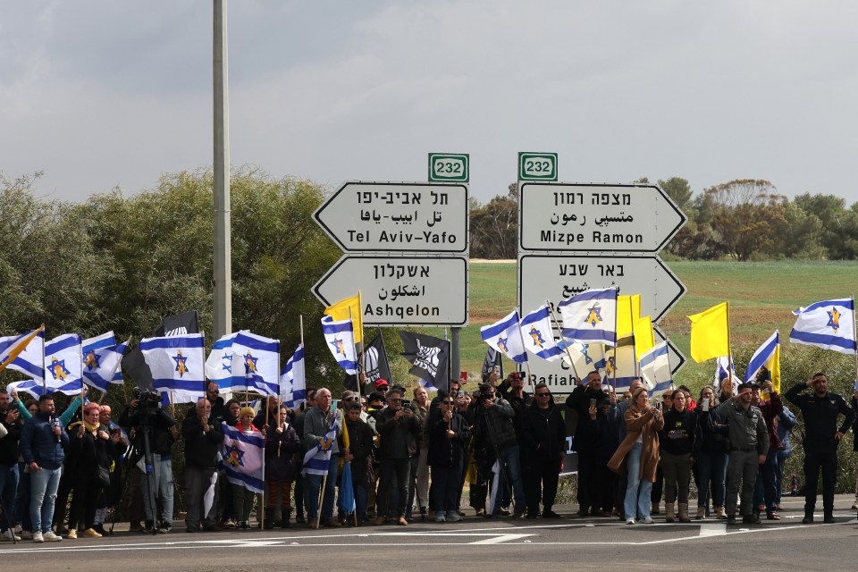 Protestors holding Israeli flags at a road sign.