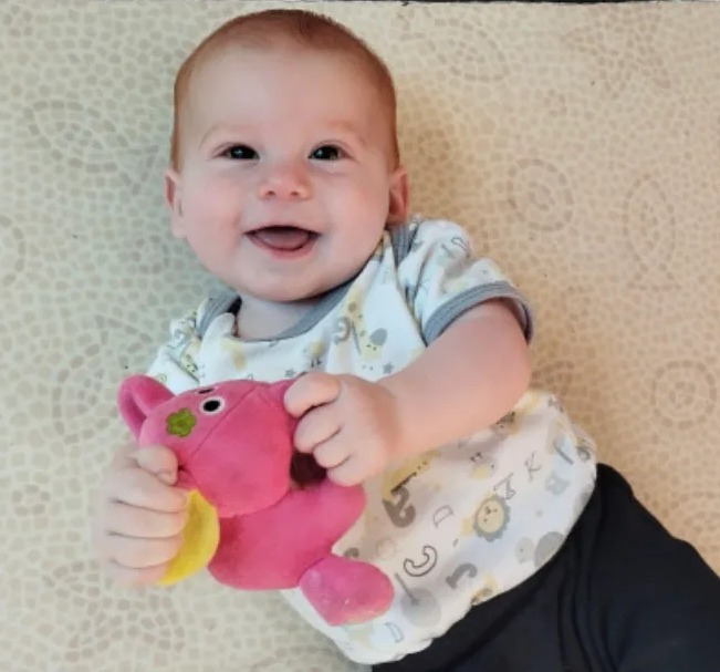 Smiling baby holding a pink stuffed animal.