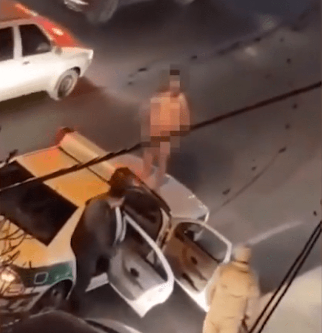 A naked man near police officers and cars.