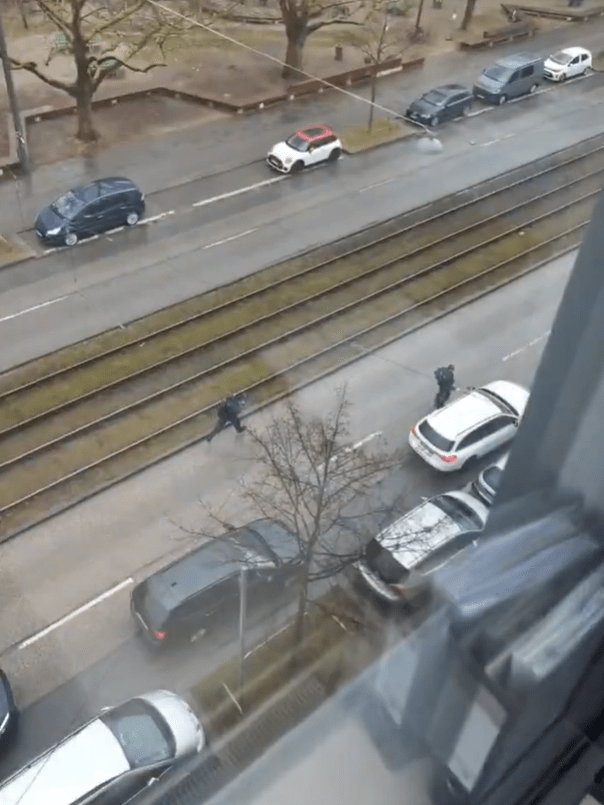 High-angle view of police officers apprehending a suspect near parked cars and tram tracks.