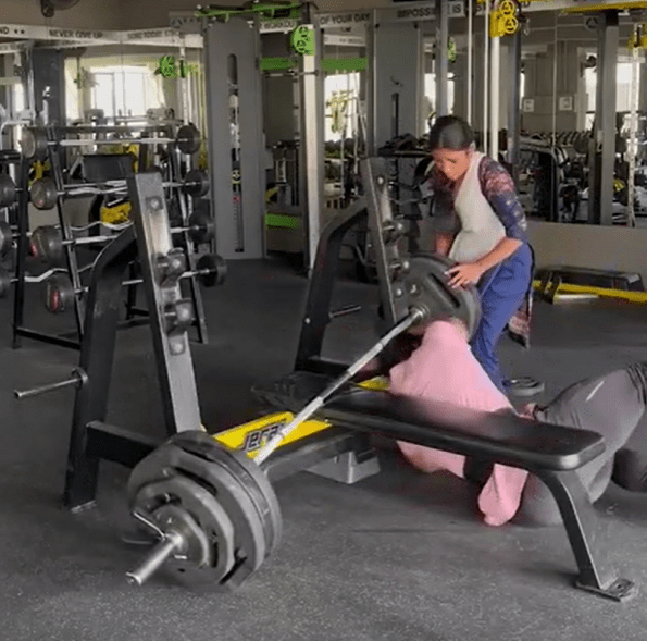 Woman assisting man with weightlifting in gym.