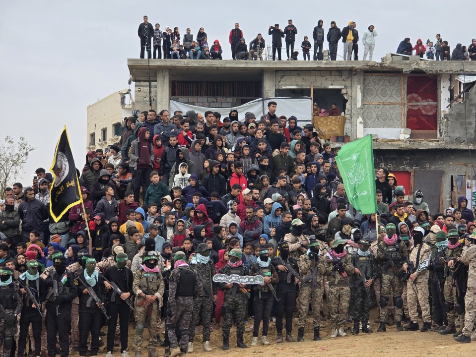 Large group of people, many in military uniforms, gathered in front of a damaged building.