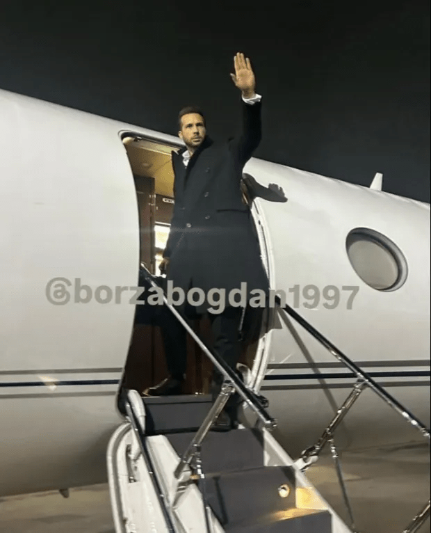 Man in a suit exiting a private jet, waving.