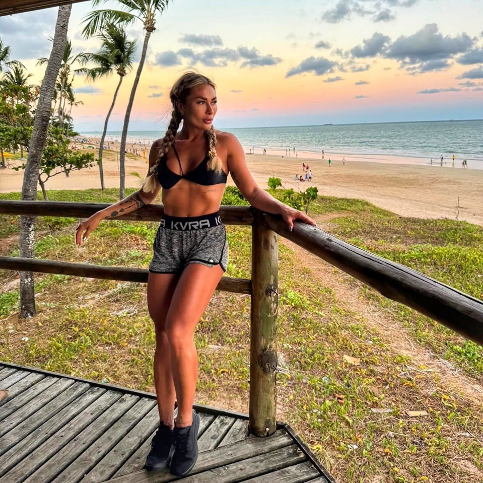 Woman in athletic wear posing on a deck overlooking a beach at sunset.