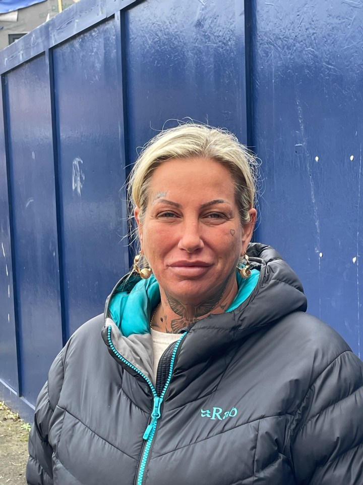 Woman in a black puffer jacket standing in front of a blue wall.