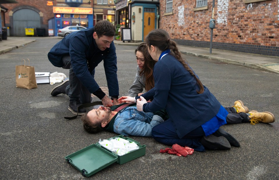 A man lies bleeding on the ground as several people attend to him.