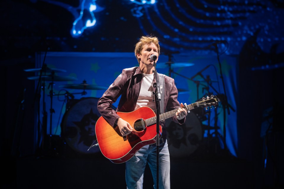 James Blunt performing on stage with an acoustic guitar.