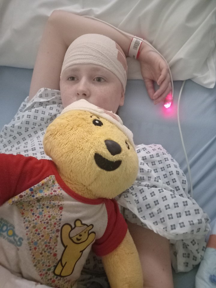 Teenage girl in hospital bed with head bandage and stuffed animal.