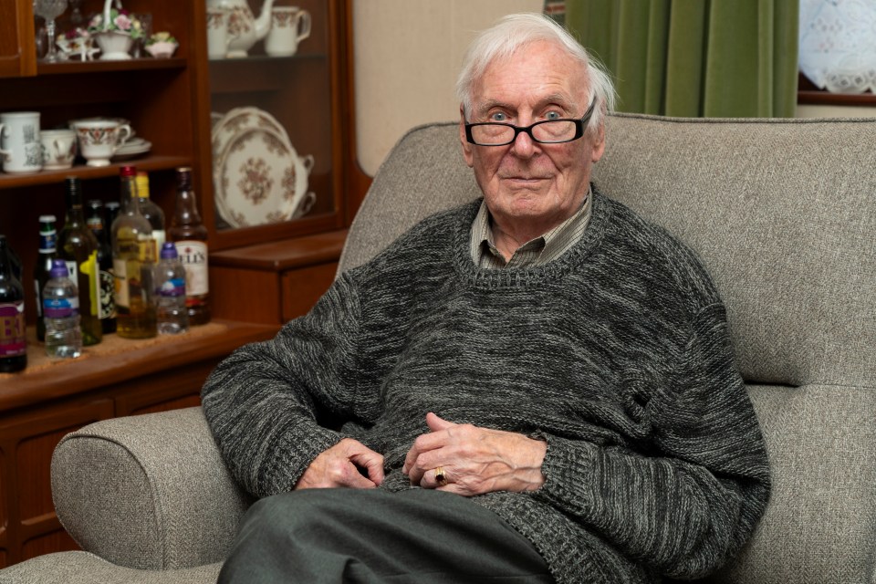 Older man in a gray sweater sitting in an armchair.