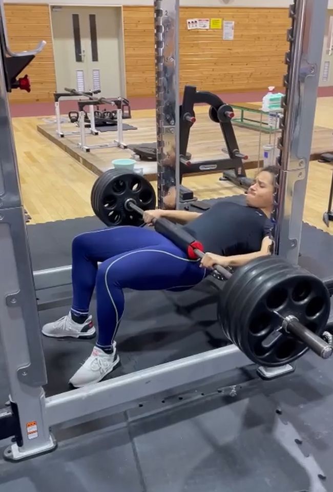 Woman performing barbell hip thrusts in a gym.