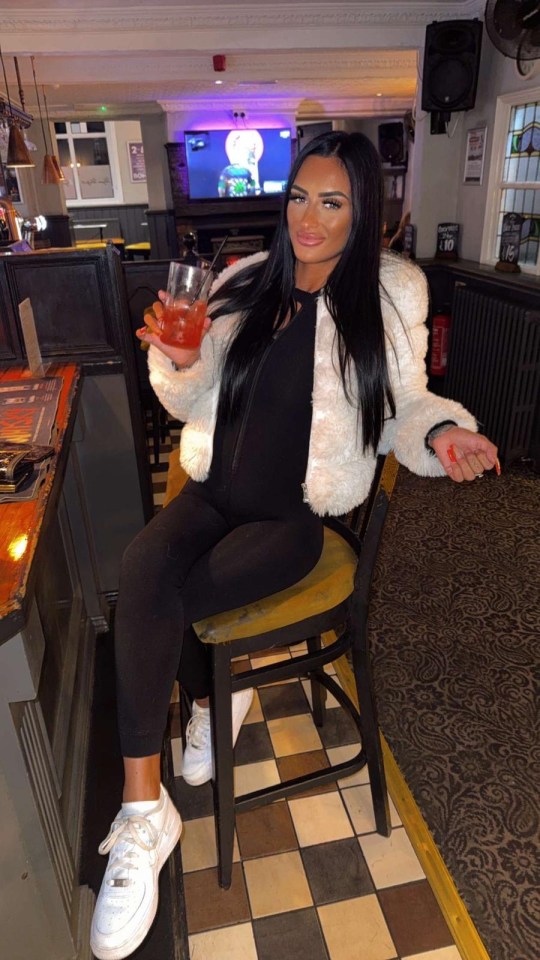 A woman sitting on a bar stool, holding a drink.