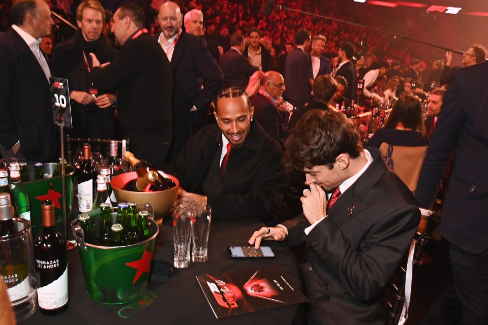 Lewis Hamilton and Charles Leclerc at an event, looking at a phone.