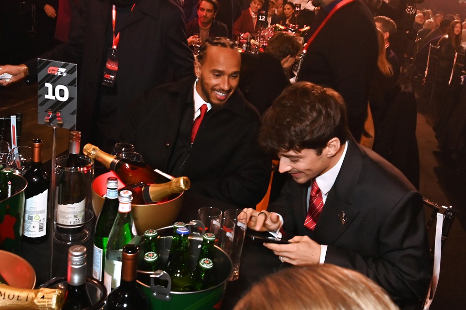 Lewis Hamilton and Charles Leclerc at a table with drinks.