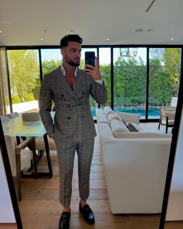 Man in a plaid suit taking a selfie in his living room.