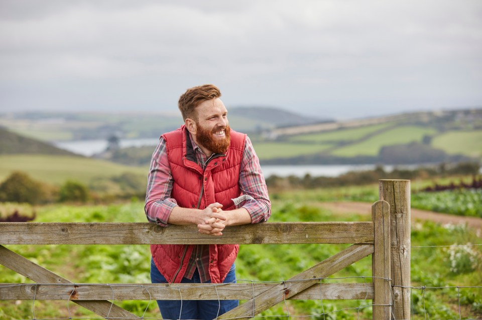 Smiling farmer leaning on a wooden gate, looking out over his farm.