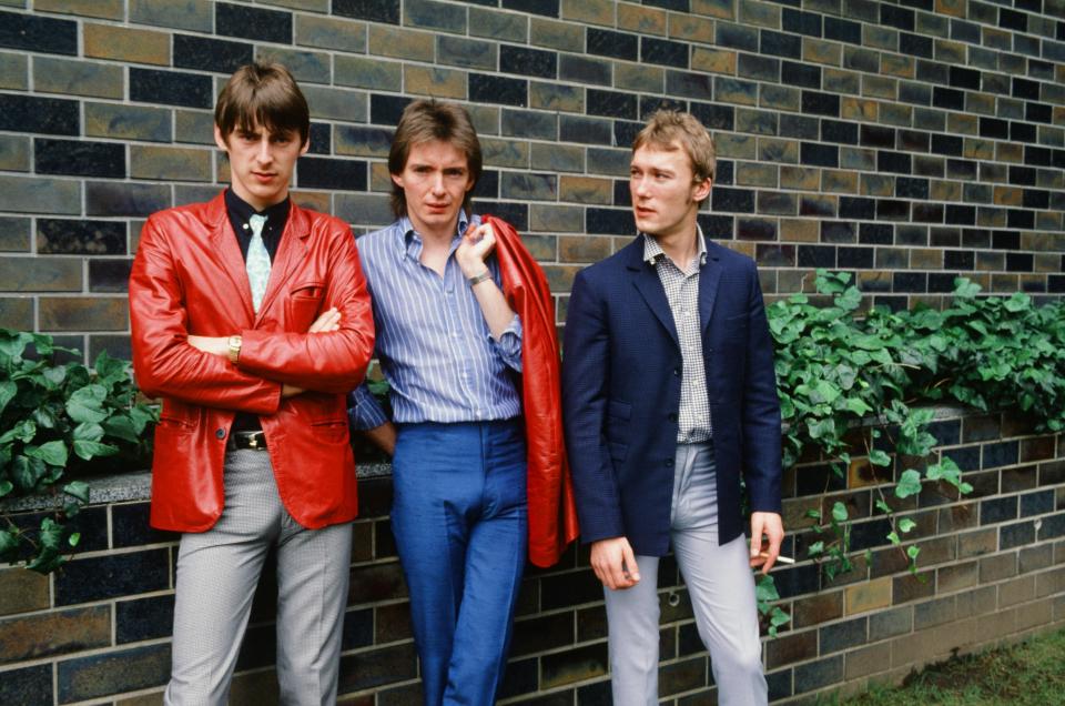 The Jam band members Paul Weller, Bruce Foxton, and Rick Buckler posing against a brick wall.