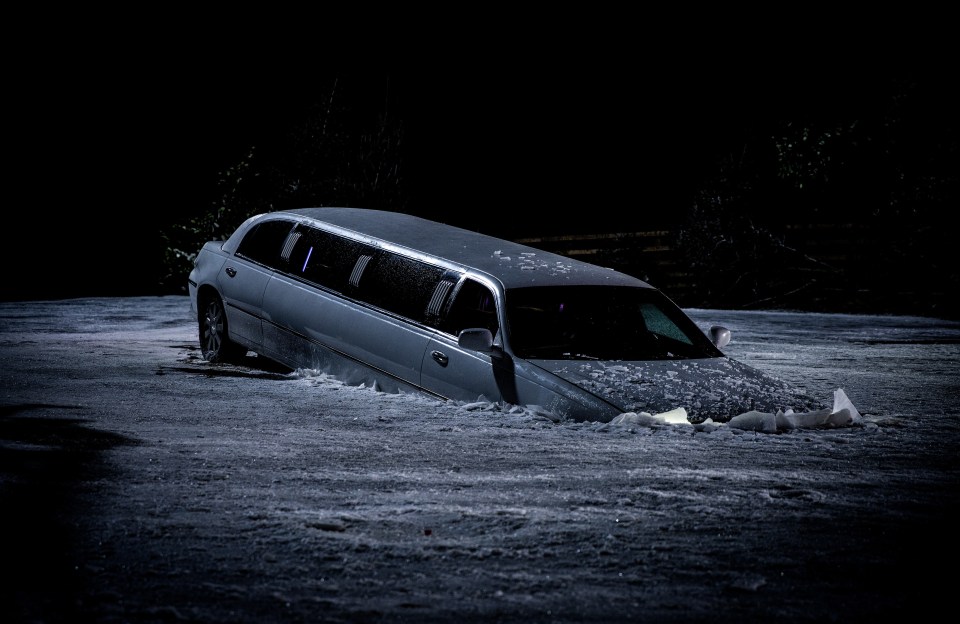 Limousine partially submerged in a frozen lake at night.