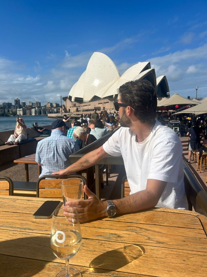 Man sitting at an outdoor table with drinks, overlooking the Sydney Opera House.