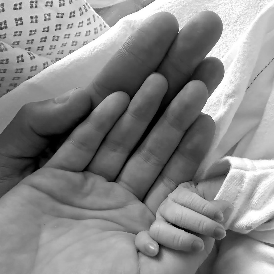 Black and white photo of an adult's hand holding a newborn's hand.