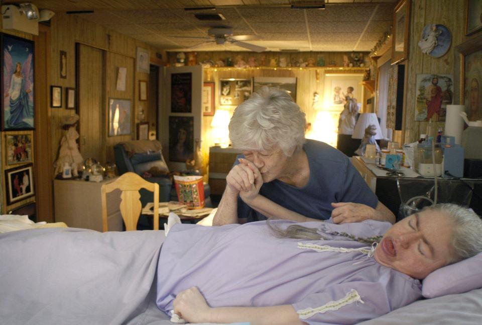 A mother kisses her daughter's hand; the daughter is lying in bed.