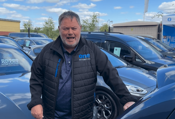 Man in One Automotive jacket standing in front of cars.