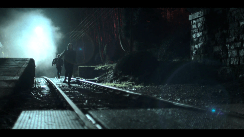 Two figures running away on a train track at night.