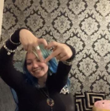 Portrait of a smiling young woman with blue hair making a heart shape with her hands.