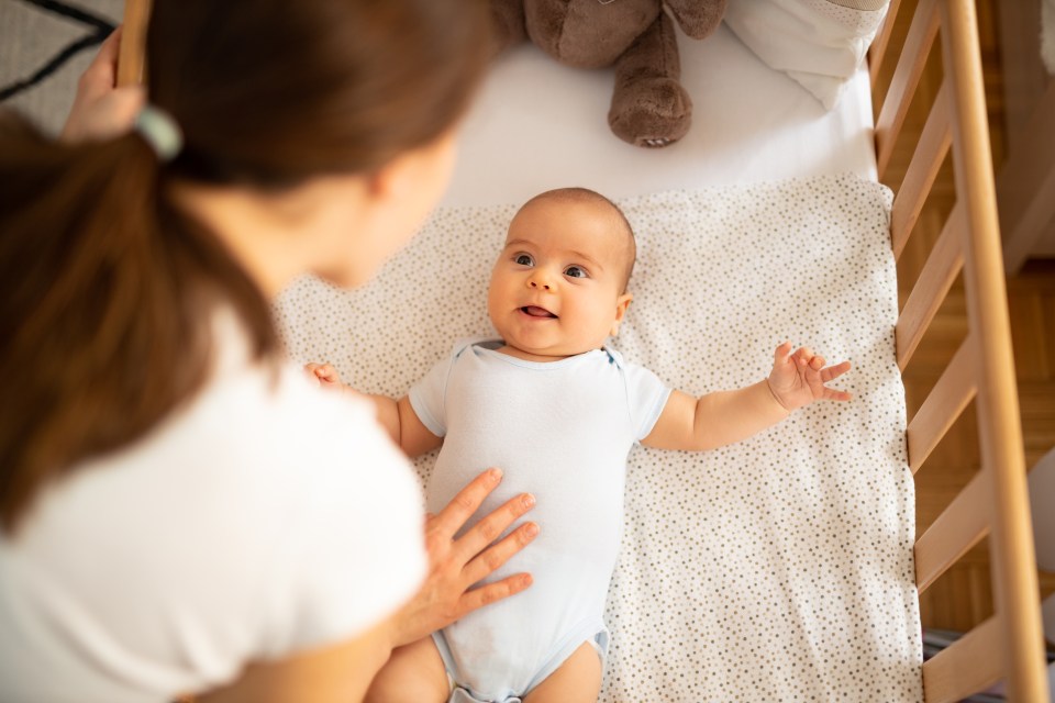 Mother leaning over crib, talking to her smiling baby boy.