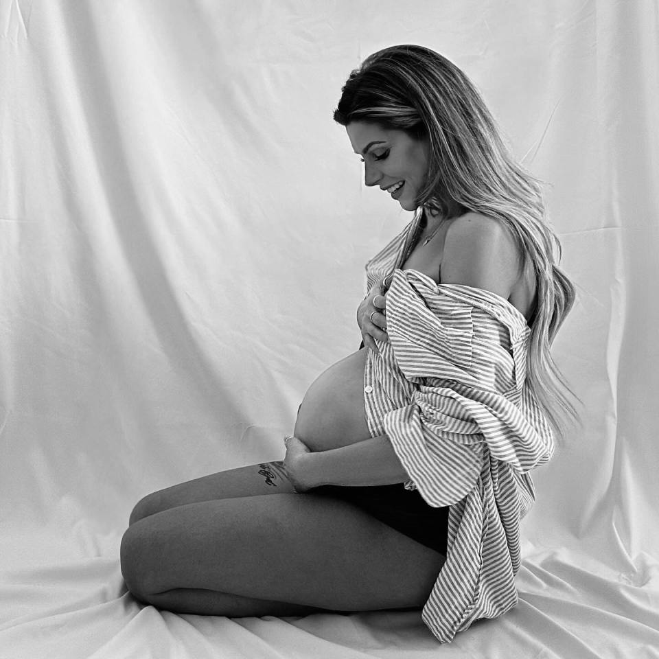 Black and white photo of a pregnant woman sitting and holding her belly.