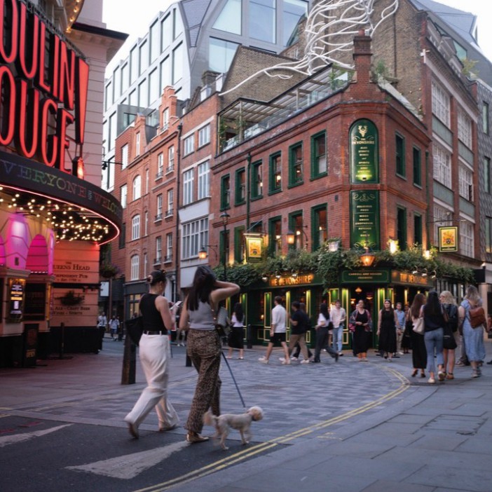 Two women walking a small dog past a pub in London.