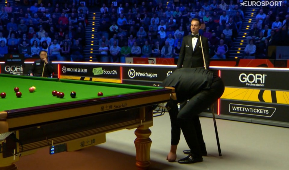 Snooker player bending down to look under the snooker table.