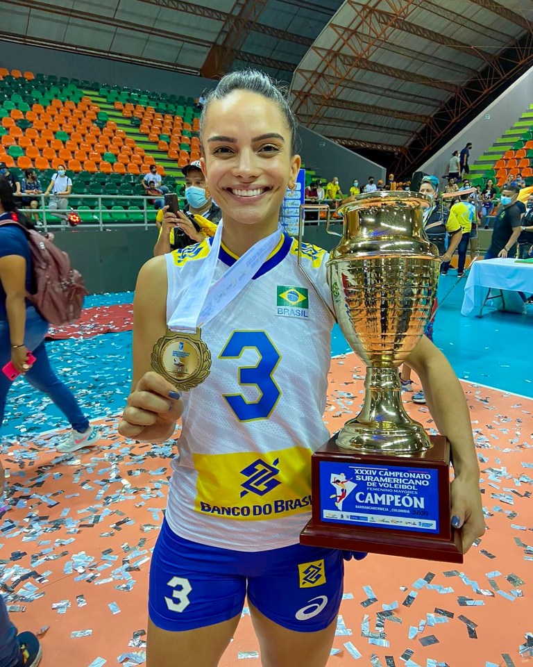 Volleyball player holding a gold medal and trophy.