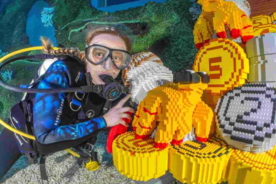 A scuba diver interacting with a large Lego structure underwater.