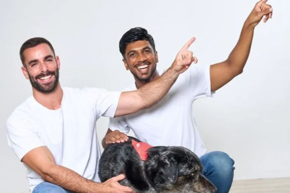 Two men and a dog sitting together.  One man is pointing.