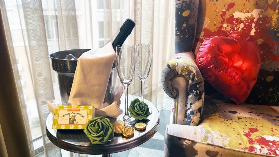 Champagne, chocolates, and roses on a side table next to an armchair.