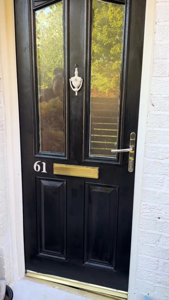 Black front door with gold doormat and number 61.