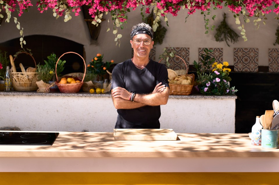 Gino D'Acampo standing in a kitchen with arms crossed.