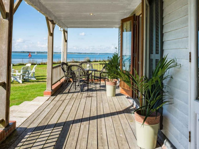 Wooden deck overlooking a body of water with lawn chairs and potted plants.