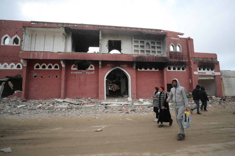 Palestinians walking past the damaged Aldeira Hotel in Gaza City.