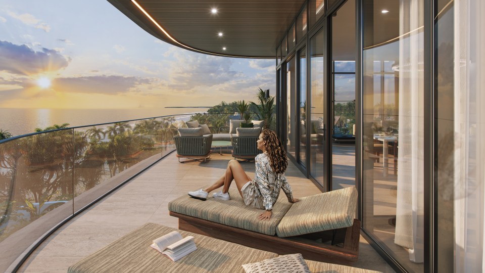 Woman relaxing on penthouse balcony overlooking ocean at sunset.