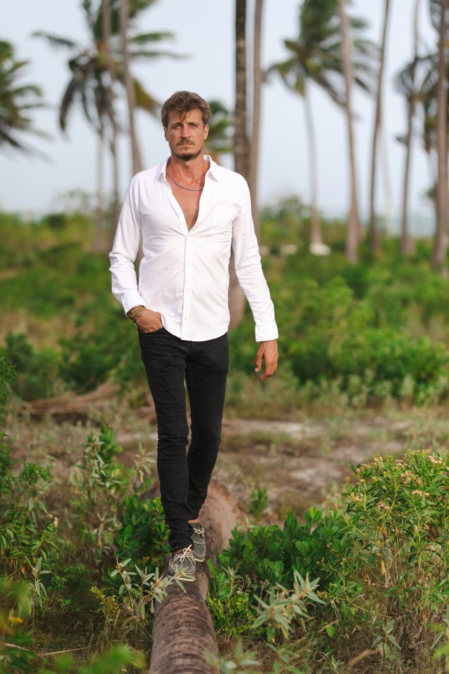 Man in white shirt walking on a log in a tropical setting.