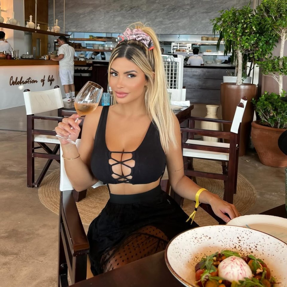 Woman in black top and skirt holding a glass of wine at a restaurant.