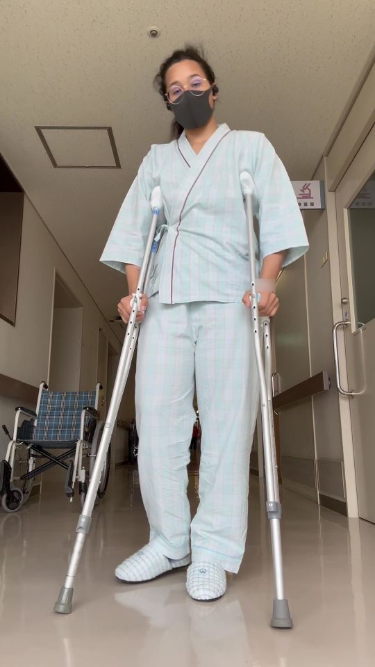 Woman in hospital gown using crutches.