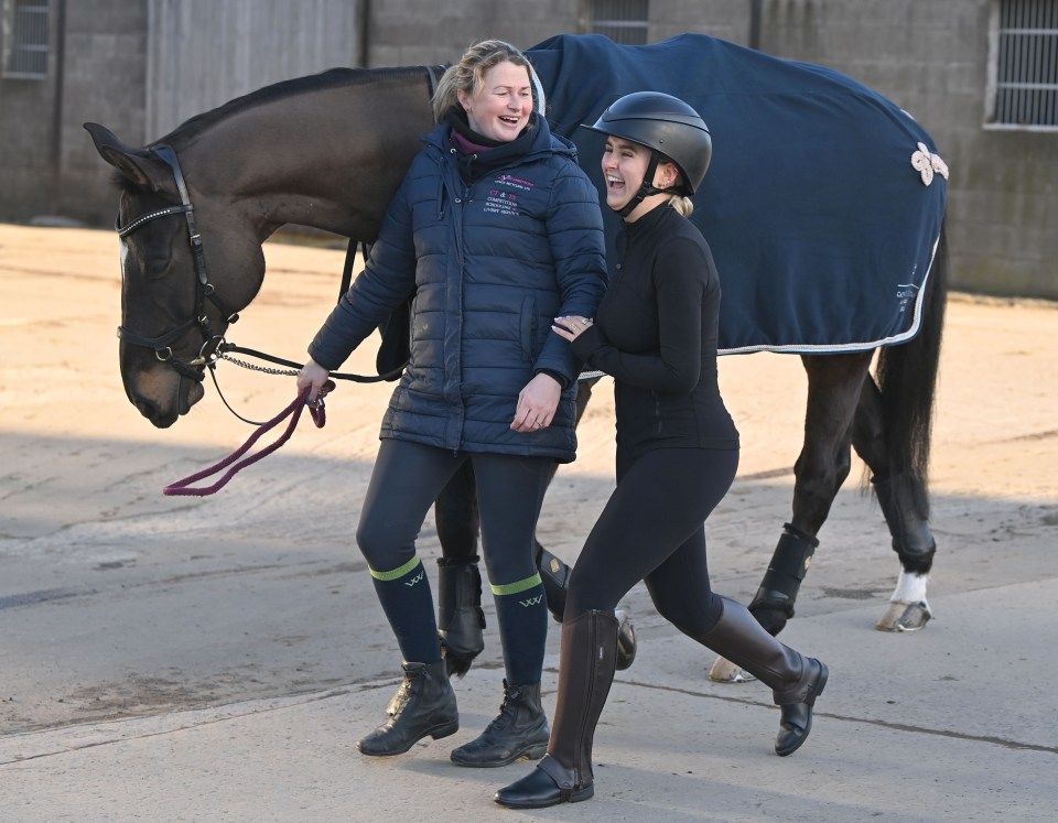 Two women laughing while leading a horse.