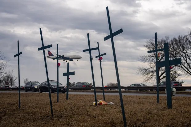 Memorial crosses near a highway with a plane overhead.